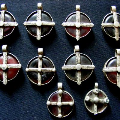 A collection of  pendants, worn around the neck. Made of a setting of low-grade silver and with an inserted sliced bead made of phenolic resin in a reddish colour. Gurage-people. Central-Ethiopia.
